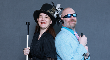 Amy and Nathan smile widely together for a photo. Both hold their long white canes.
