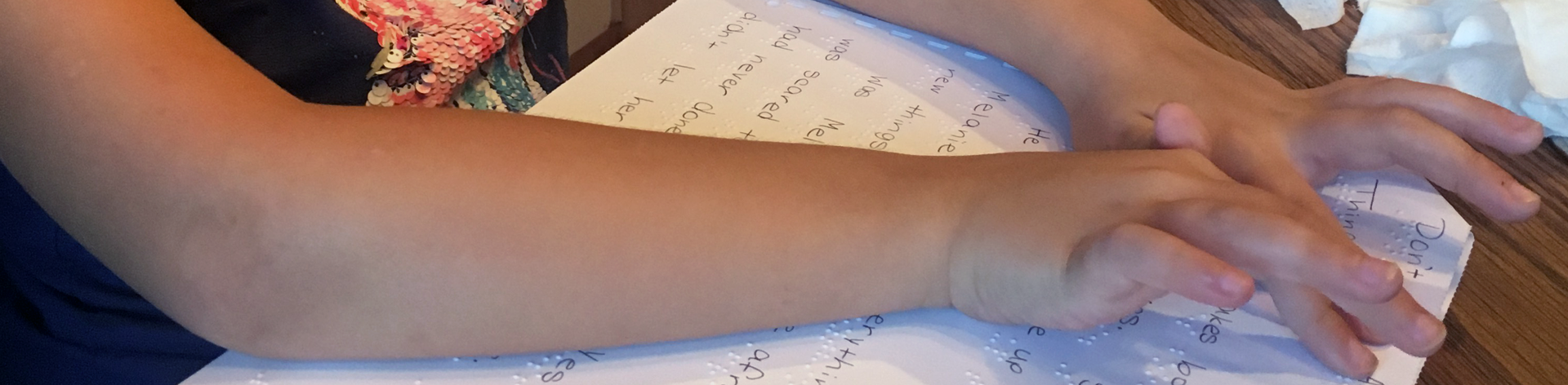 Close-up of a child's hands reading a Braille/print page.